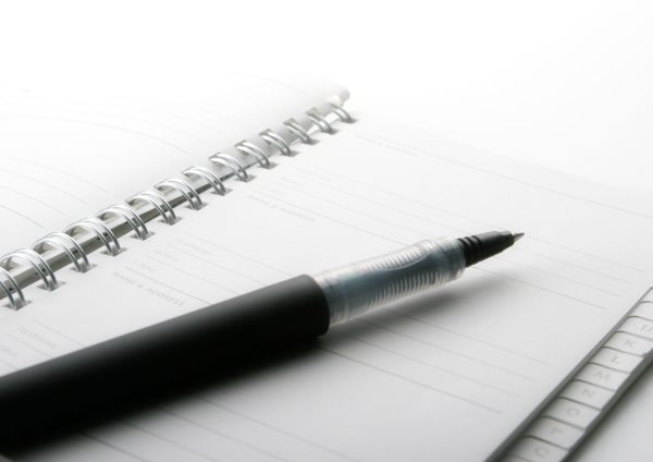 A close up macro view of a wire bound notebook and pen