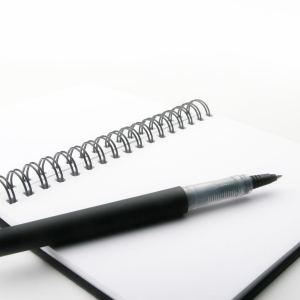 A close up macro view of a wire bound notebook and pen