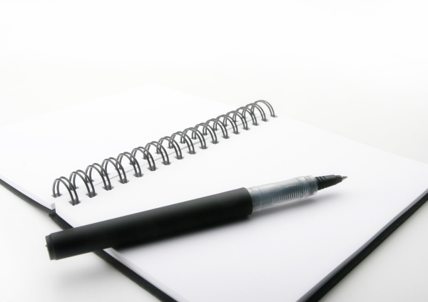 A close up macro view of a wire bound notebook and pen