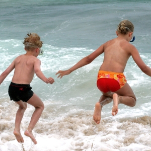 Young boy and girl jumping into the surf on a seaside holiday and having fun