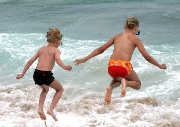 Young boy and girl jumping into the surf on a seaside holiday and having fun