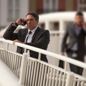 A man on a bridge, watching and communicating on his mobile phone