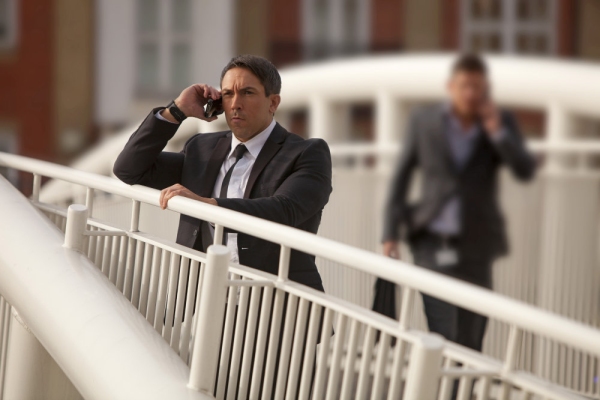 A man on a bridge, watching and communicating on his mobile phone