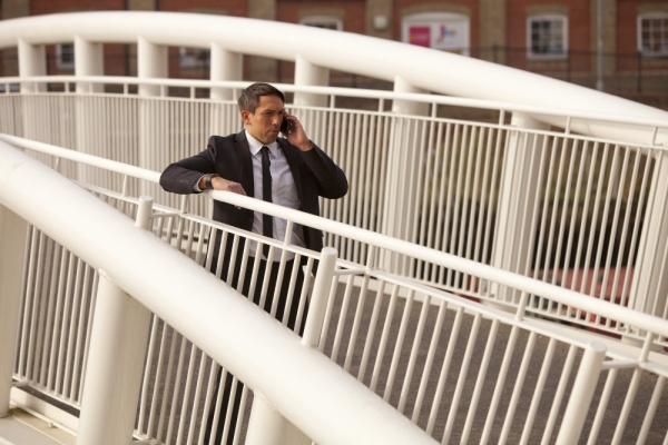 A tough looking security man talking on a mobile phone in an urban environment on a bridge