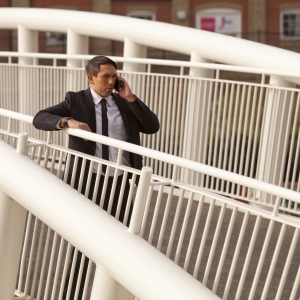 A tough looking security man talking on a mobile phone in an urban environment on a bridge