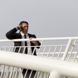 A man in a suit talking on his mobile while watching from a bridge