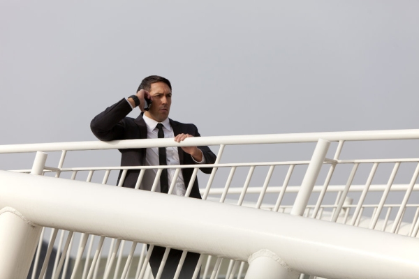 A man in a suit talking on his mobile while watching from a bridge