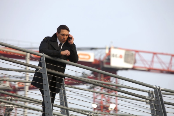 A security guard looking down with a large building site crane in the background