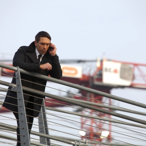 A security guard looking down with a large building site crane in the background