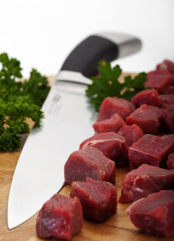 Chopped braising steak on a chopping board with carving knife. Out of focus background