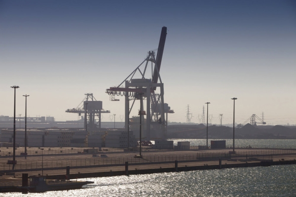 Cranes and containers at a modern dock terminal, with older heavy industry installations in the background