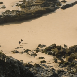 Walkers on a flat sandy beach with large rock formations