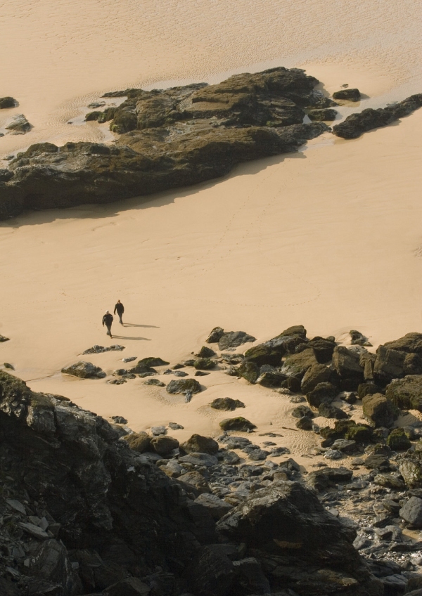 Walkers on a flat sandy beach with large rock formations