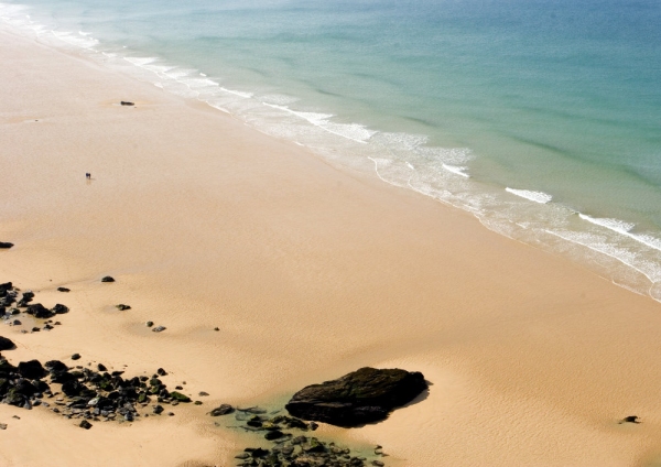 The shoreline on a wide, sandy beach with rocks in the foreground