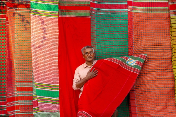 A Bangladeshi vendor sits under his display of traditional towels or gamcha as he waits for customers on a street of Dhaka.