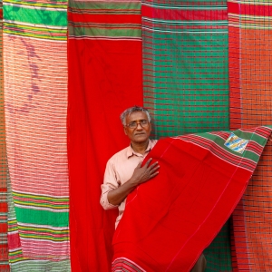 A Bangladeshi vendor sits under his display of traditional towels or gamcha as he waits for customers on a street of Dhaka.