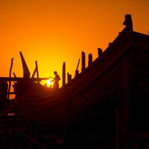 In the last light of Twilight, a craftsmen passing busy time in making on wooden boat at Noakhali, Bangladesh. According to the boat makers, the dry season, especially from December to June, is the ideal time for making the fishing boats. Craftsmen are hammering the nail in the wooden body of the ship and they are working till the end because the ships will have to float in the sea shortly after them.