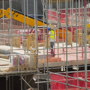 A building site worker or hod carrier or labourer carrying bricks on a building site with scaffolding