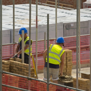 Two bricklayers or construction workers laying bricks on a new greenfield housing development with scaffolding and safety netting