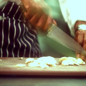 A chef or sous chef in a restaurant kitchen preparing mushrooms on a wooden chopping board