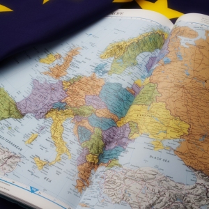 An atlas showing the map of Europe and the Mediterranean with a European Union flag in the background