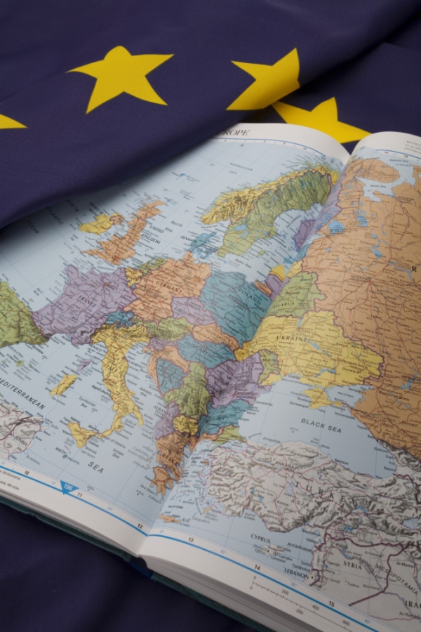 An atlas showing the map of Europe and the Mediterranean with a European Union flag in the background