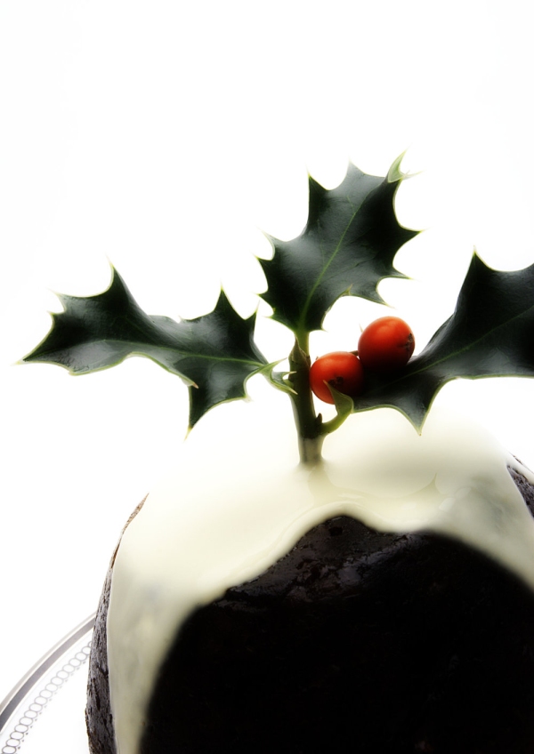 A Christmas pudding with cream and a sprig of holly on top