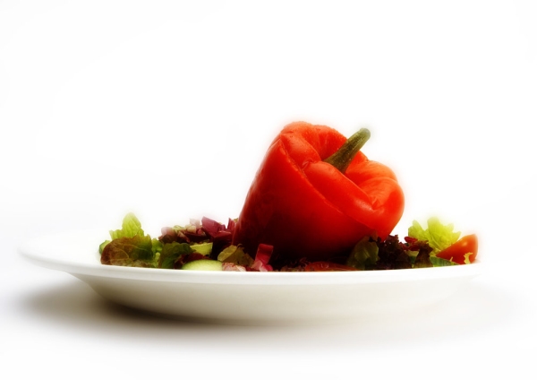 A stuffed red pepper with a green salad on a white plate