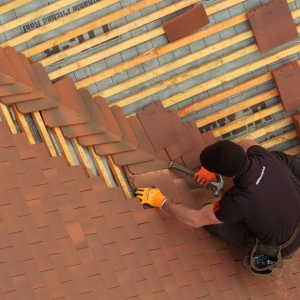 A drones eye view of a tiler finishing of a traditional red tiled roof