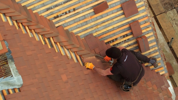 A drones eye view of a tiler finishing of a traditional red tiled roof