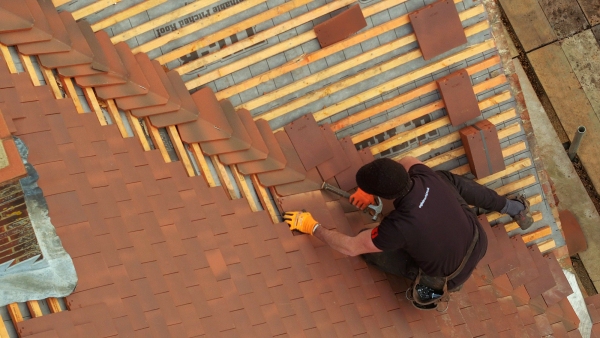 A drones eye view of a tiler finishing of a traditional red tiled roof