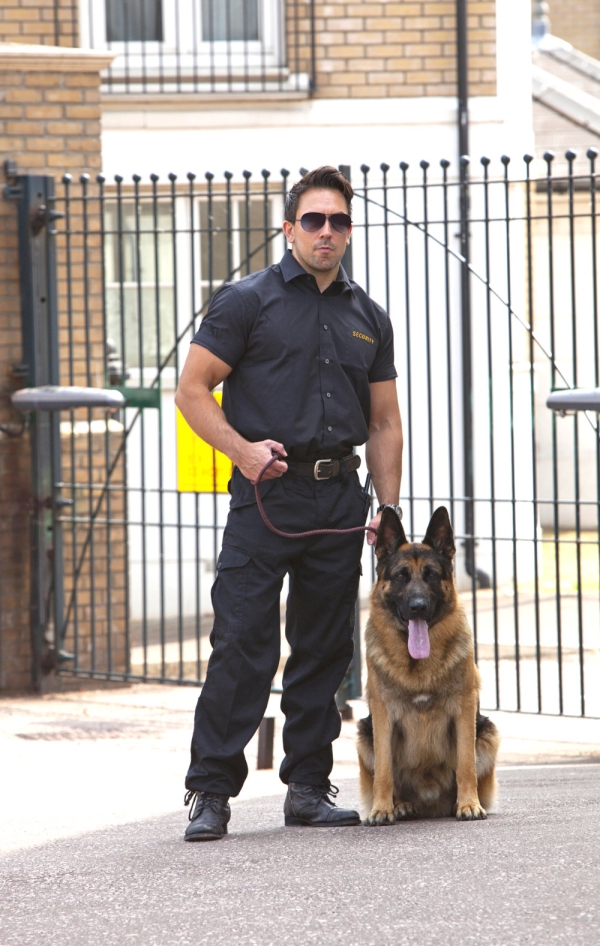 Security guard with German Shepherd guard dog in front of security gates