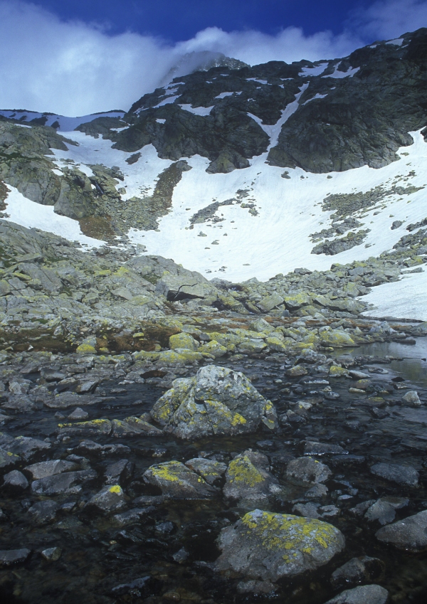 Snow covered mountains in the Italian alps, with a rocky stream in the foreground