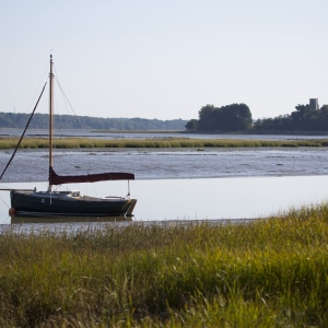 A traditional wooden hulled sailing boat moored at low tide in the Alde estuary with Iken church in the background