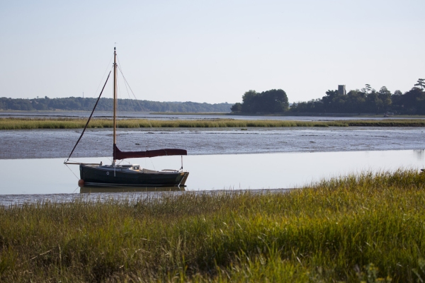 A traditional wooden hulled sailing boat moored at low tide in the Alde estuary with Iken church in the background