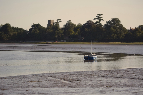 A small sailing boat moored in the estuary at low tide on the River Alde near Snape Maltings