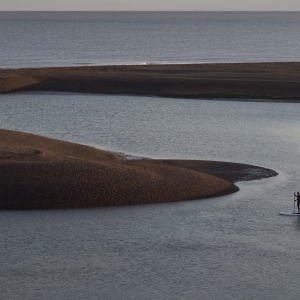 A lone paddle boarder at low tide at Shingle Street in Suffolk