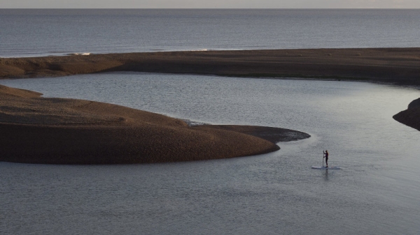 A lone paddle boarder at low tide at Shingle Street in Suffolk