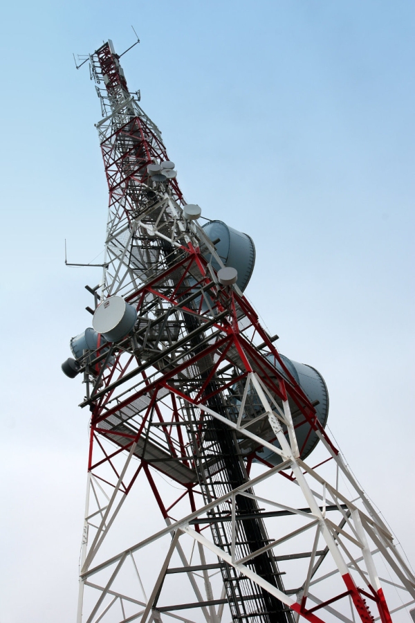 A communications mast with satellite dishes agains a blue sky