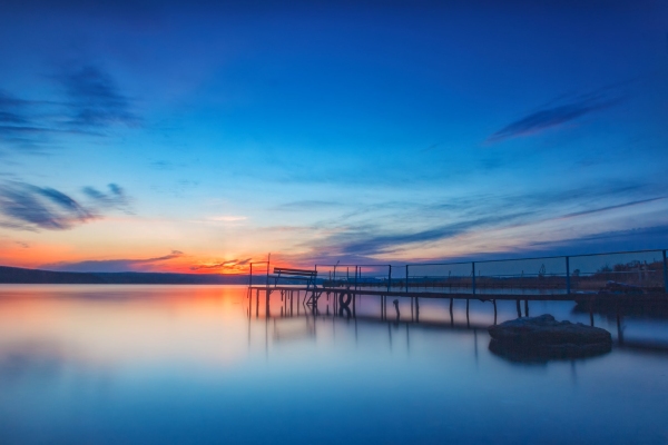 Amazing long exposure sunset on the lake with a bench on the wooden pier.