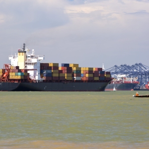 A large container ship being guided into port by pilot tugs