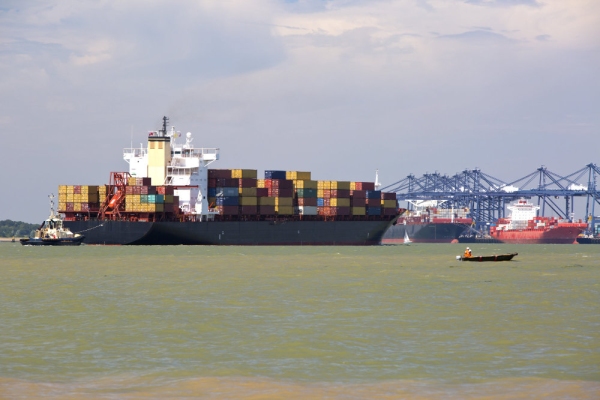 A large container ship being guided into port by pilot tugs