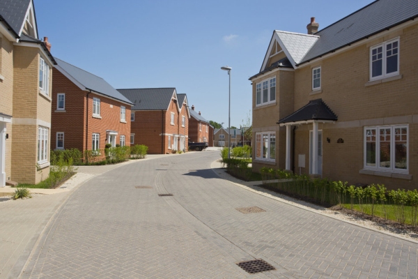 An empty street in a mostly complete new housing development, with houses sold before completion