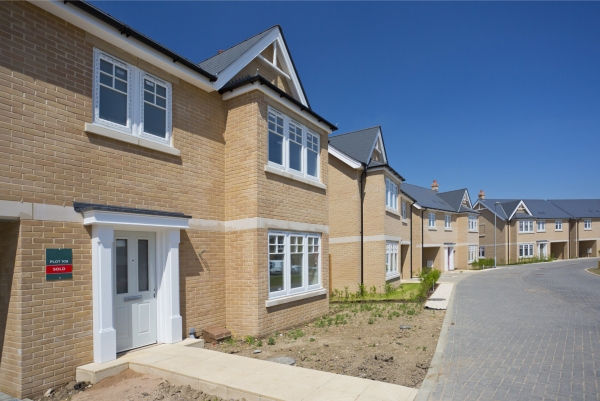 An empty street in a mostly complete new housing development, with houses sold before completion