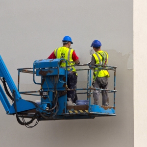 two plasterers working on the wall of a new building from a cherry picker or lift platform