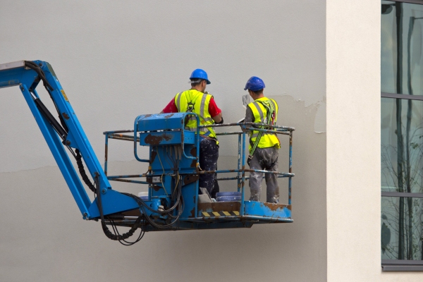 two plasterers working on the wall of a new building from a cherry picker or lift platform