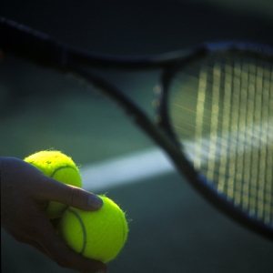 Tennis balls and a racquet in the hands of a player about to serve