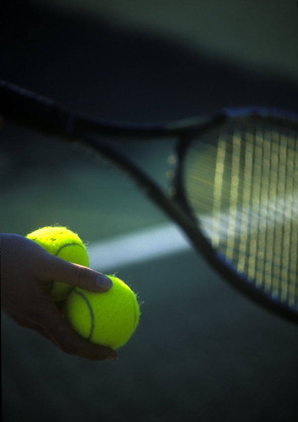 Tennis balls and a racquet in the hands of a player about to serve