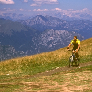 A cyclist on a mountain bike in a high alpine setting, with mountains in the background