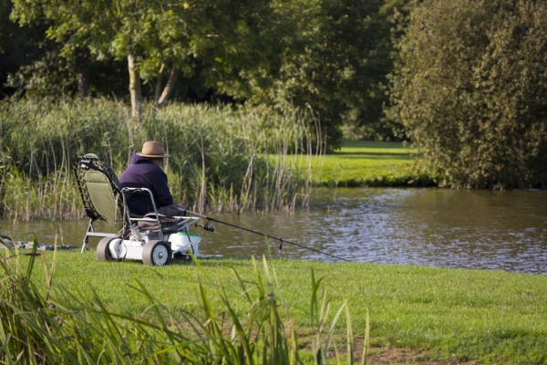 An elderly angler carp fishing on a summer lake in Suffolk, with electric assisted bait trolley